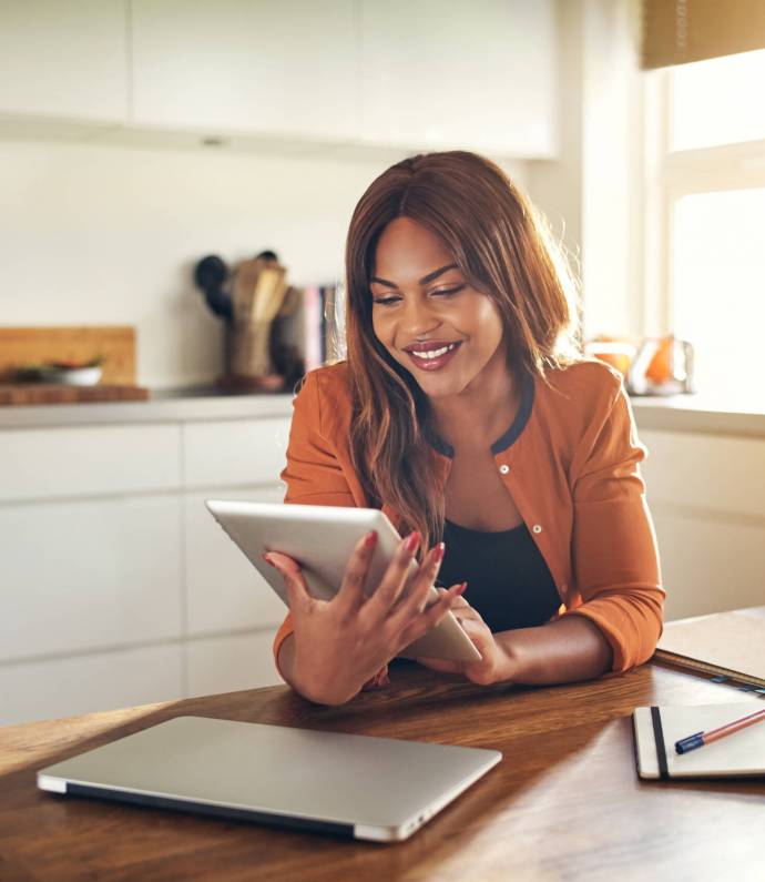 Smiling young African female entrepreneur working online with a digital tablet while sitting at a table in her kitchen